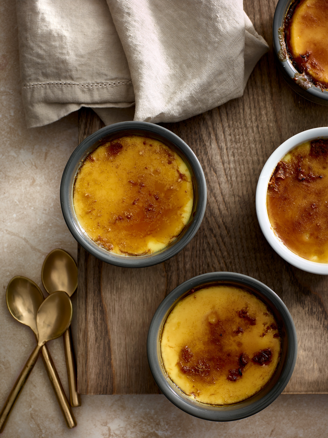 Three creme brulee desserts with golden spoons